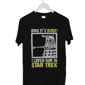 May include: Black t-shirt with a humorous graphic featuring a Dalek-like robot and the text "OMG IT'S R2D2! I LOVED HIM IN STAR TREK" in white and yellow. The shirt is hanging on a white hanger.