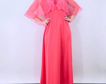 May include: A coral-colored vintage maxi dress with a matching sheer capelet. The dress features a V-neckline and a flowing skirt. The capelet has a scalloped edge and a tie closure at the neckline. The dress is a vibrant, solid color.