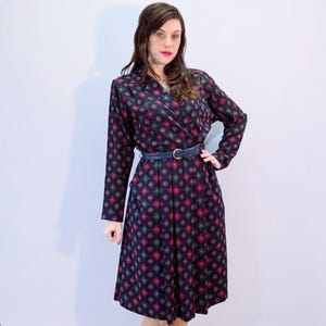 Könnte beinhalten: Ein marineblaues Wickelkleid mit langen Ärmeln und einem sich wiederholenden Muster aus roten und grünen Rauten. Das Kleid wird mit einem blauen Gürtel in der Taille zusammengehalten und hat einen V-Ausschnitt. Das Kleid ist knielang.