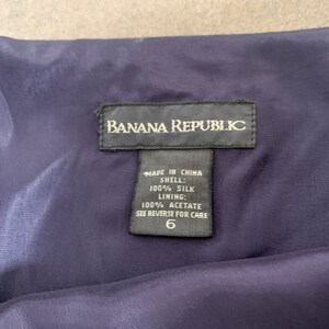 May include: A black tag with white text that reads "Banana Republic" and "Made in China" with the fabric composition and care instructions. The tag is attached to a dark blue fabric.