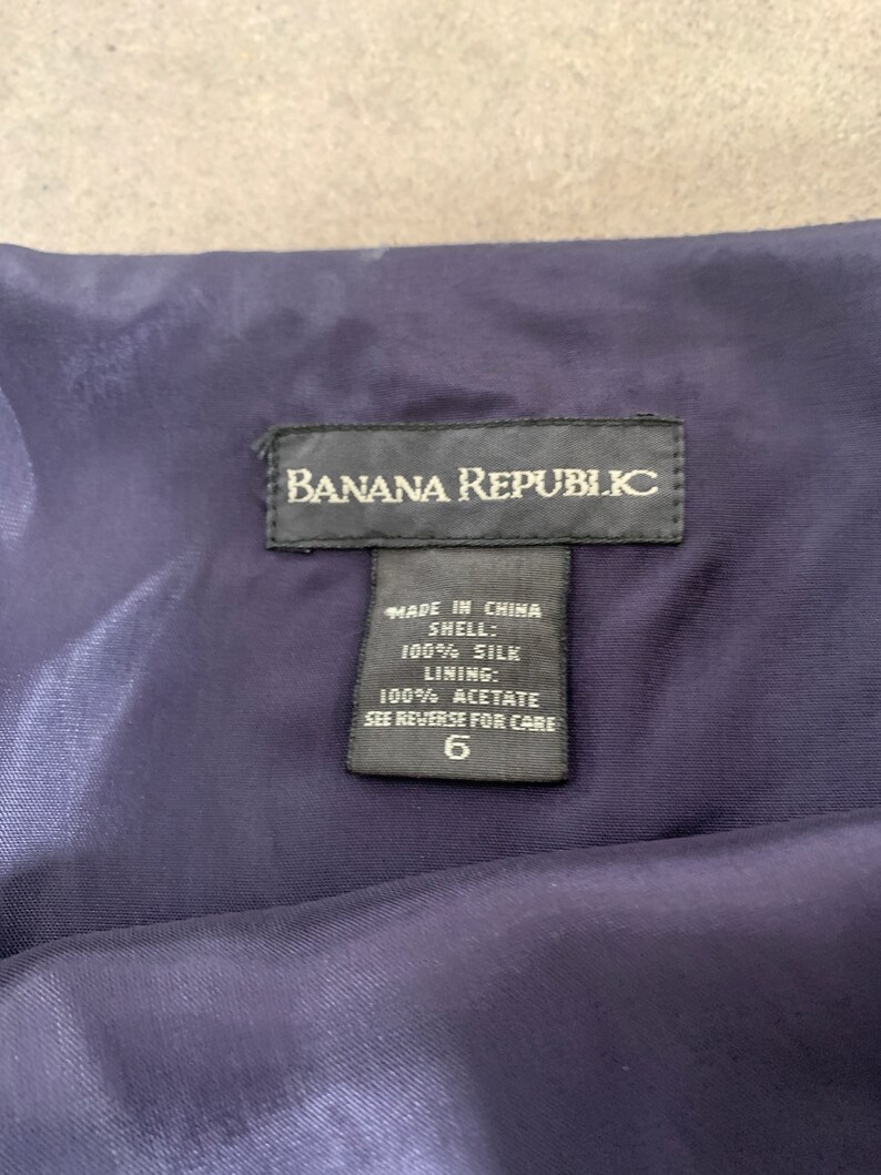 May include: A black tag with white text that reads "Banana Republic" and "Made in China" with the fabric composition and care instructions. The tag is attached to a dark blue fabric.