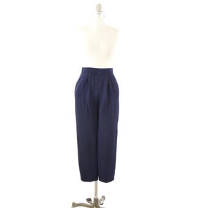 May include: A pair of high-waisted navy blue trousers featuring a pleated front design, a structured waistband, and a straight-leg silhouette that extends to the ankles, displayed on a neutral-toned mannequin torso for clear visibility.
