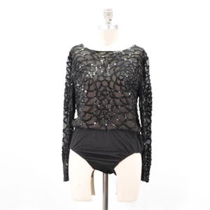 May include: A long-sleeved black bodysuit featuring a sheer mesh overlay adorned with intricate black sequin patterns in a scalloped design. The garment has a round neckline and a solid black lower section, providing a cohesive look with consistent sequin detailing across the sleeves and bodice.