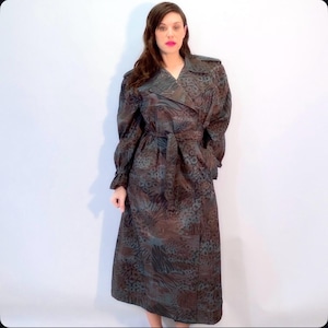 May include: A long, patterned trench coat in shades of brown, teal, and black. The coat features a double-breasted design, a belted waist, and long sleeves. The fabric has a subtle sheen, and the overall style is vintage-inspired.