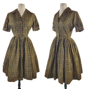 May include: A vintage 1950s dress with a black and gold geometric print. The dress has a button-up front, short sleeves, and a full skirt.