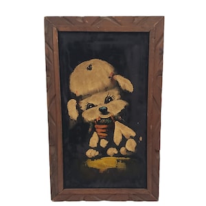 May include: A framed painting of a white poodle wearing a red bow and a hat, sitting on a yellow background. The painting is on a black velvet background.