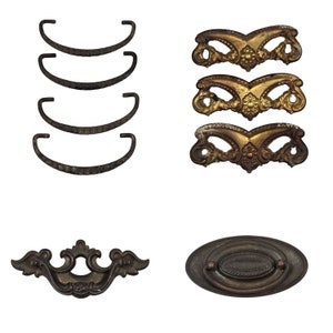 Op de afbeelding: Assortiment van antieke ladetrekkers in verschillende stijlen. Vier eenvoudige, zwarte metalen trekkers met een gebogen vorm. Drie sierlijke, goudkleurige trekkers met een decoratief bloemenmotief. Een ovale, zwarte metalen trekker met een verhoogd midden.