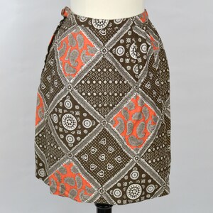 May include: A brown and orange patterned skirt with a geometric design. The skirt is made of a lightweight fabric and has a wrap-around style.
