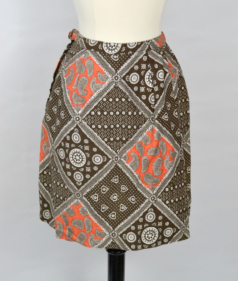 May include: A brown and orange patterned skirt with a geometric design. The skirt is made of a lightweight fabric and has a wrap-around style.