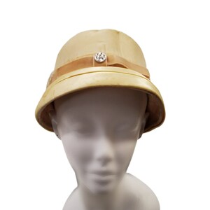 May include: A beige hat with a wide brim and a decorative rhinestone button. The hat is made of a smooth, shiny material.
