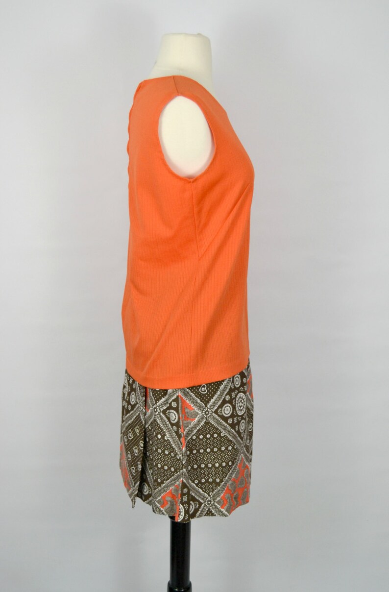 May include: A sleeveless orange top with a brown and white patterned skirt. The skirt has a geometric design with a paisley pattern.