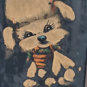 May include: A painting of a white dog wearing a brown hat and a green and orange scarf. The dog is sitting on a yellow surface against a black background.