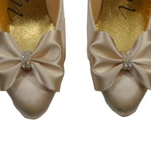 May include: A pair of ivory satin bridal shoes with a bow and rhinestone embellishment on each toe.