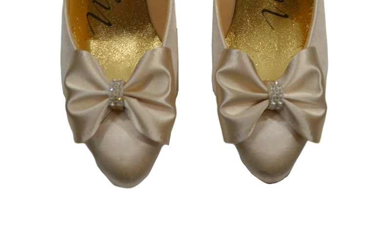 May include: A pair of ivory satin bridal shoes with a bow and rhinestone embellishment on each toe.