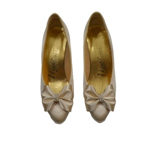 May include: A pair of ivory satin pumps with a small jeweled bow on the toe. The shoes are labeled "Night Life by Jeffrey West".