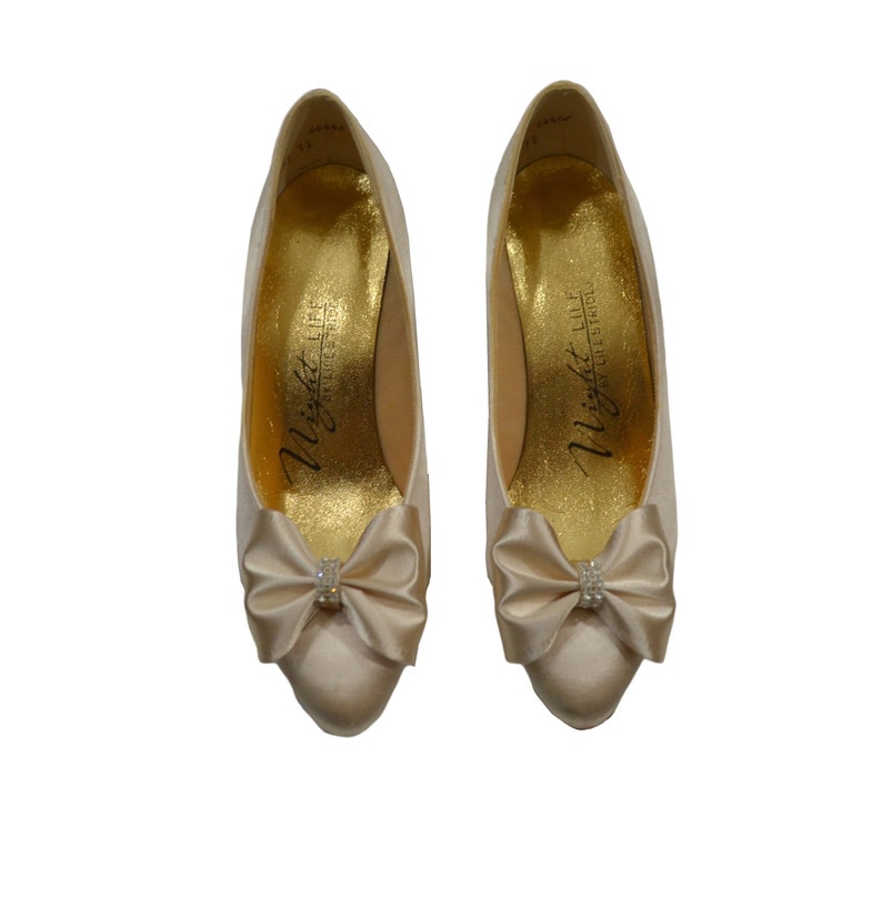 May include: A pair of ivory satin pumps with a small jeweled bow on the toe. The shoes are labeled "Night Life by Jeffrey West".