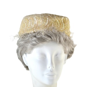 Puede incluir: Un sombrero de pastillero vintage de color marfil con un velo de red delicado y adornos de cuentas.