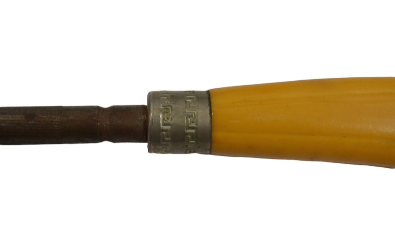 May include: A close-up of a yellow handled tool with a metal tip and a decorative band around the handle. The band has a repeating geometric pattern.