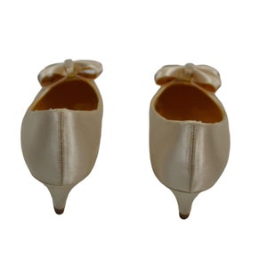 May include: A pair of ivory satin low heeled shoes with a bow on the toe.
