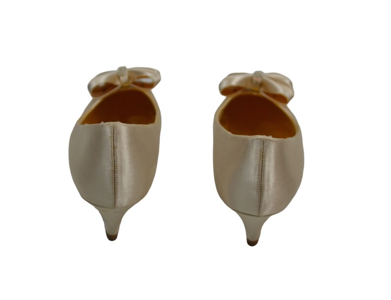May include: A pair of ivory satin low heeled shoes with a bow on the toe.