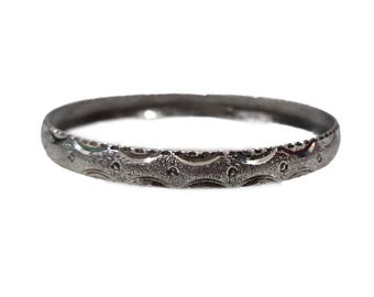 Op de afbeelding: Een zilverkleurige ring met een getextureerd oppervlak. De ring heeft een herhalend patroon van gebogen lijnen en kleine cirkels. De band is ongeveer 0,25 cm breed. De ring staat tegen een witte achtergrond.