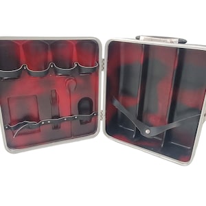 May include: A silver metal case with a red and black interior. The case has a handle and a latch. The interior has compartments for holding bottles and other items.