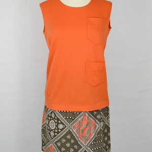 May include: A sleeveless orange dress with a brown and white patterned skirt. The dress has a pocket on the front.