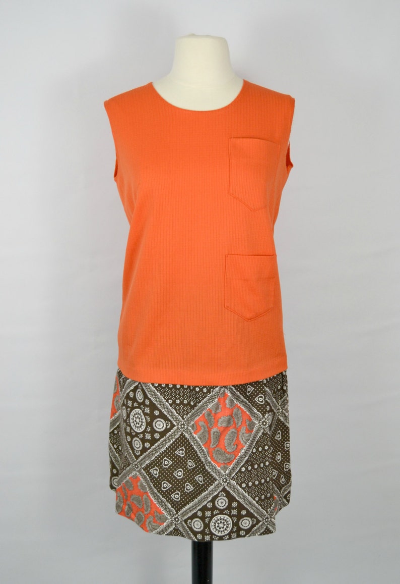 May include: A sleeveless orange dress with a brown and white patterned skirt. The dress has a pocket on the front.