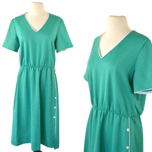 Op de afbeelding: Een turquoise blauwe jurk met een witte rand rond de halslijn en mouwen. De jurk heeft een geplooide taille en een knoopsluiting aan de zijkant.