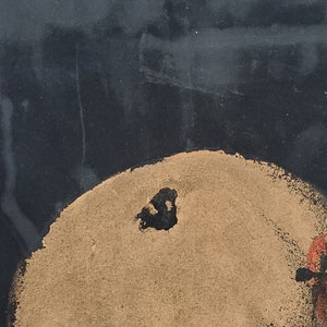 May include: A close-up of a black and gold abstract painting. The painting features a large, round, gold shape with a black centre. The background is black.