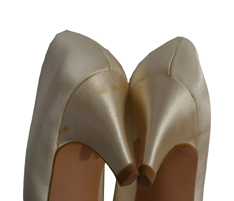 May include: A pair of ivory satin high-heeled shoes with a pointed toe.
