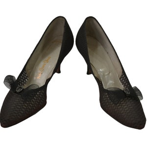 May include: A pair of black mesh heeled shoes with a bow detail on the front. The shoes are labeled "Red Cross Shoes".