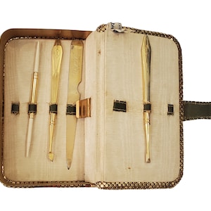 May include: A gold-colored metal manicure set with a white handle, a nail file, and a cuticle pusher. The set is in a brown and green leather case with a snap closure.