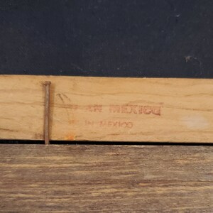 May include: Close-up of a wooden frame with a red stamp that reads "En Mexico" and "In Mexico".