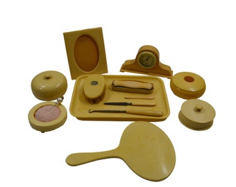 Può includere: Un set da toeletta vintage giallo, che comprende un piccolo orologio, uno specchio, una spazzola, un vassoio e diverse piccole scatole.