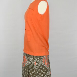 May include: A sleeveless orange top with two pockets and a brown and white patterned skirt. The skirt has a geometric design with orange accents.