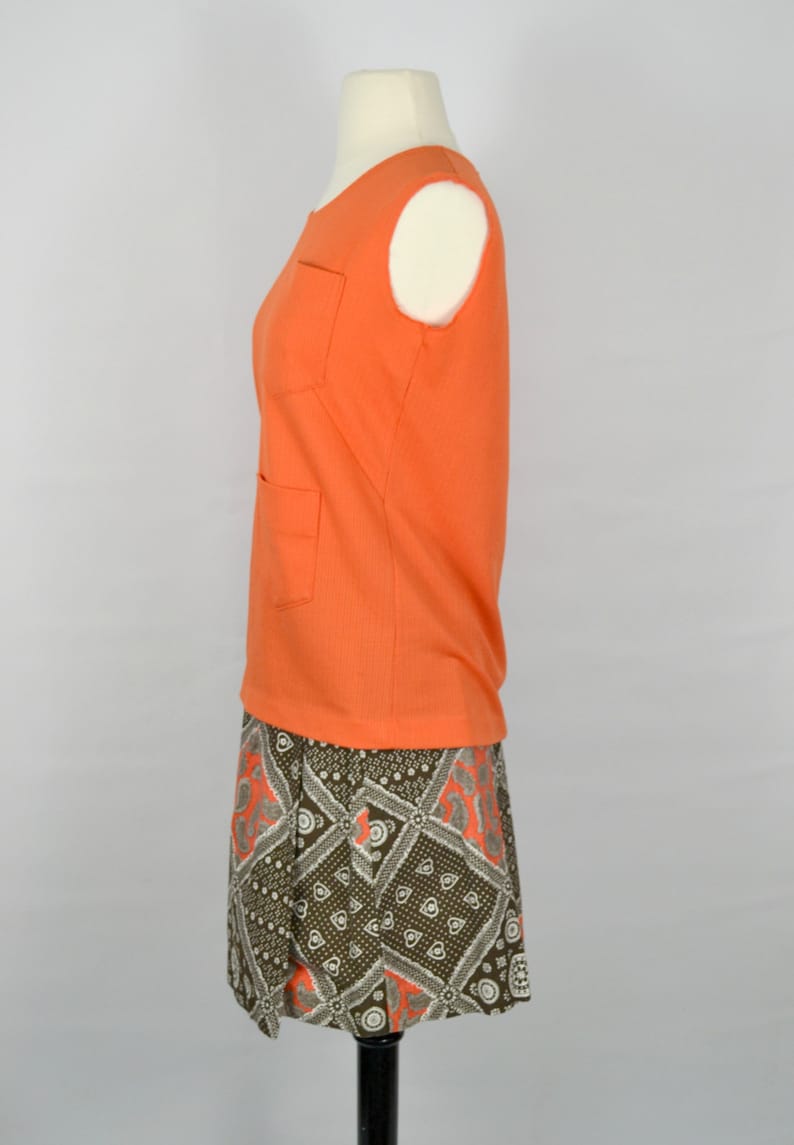 May include: A sleeveless orange top with two pockets and a brown and white patterned skirt. The skirt has a geometric design with orange accents.
