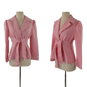 Puede incluir: Una chaqueta rosa con cinturón de lazo. La chaqueta tiene mangas largas y cuello de pico.