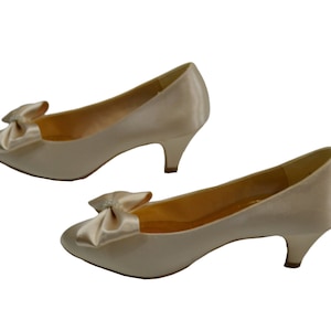 May include: A pair of ivory satin low heeled pumps with a bow detail on the toe.