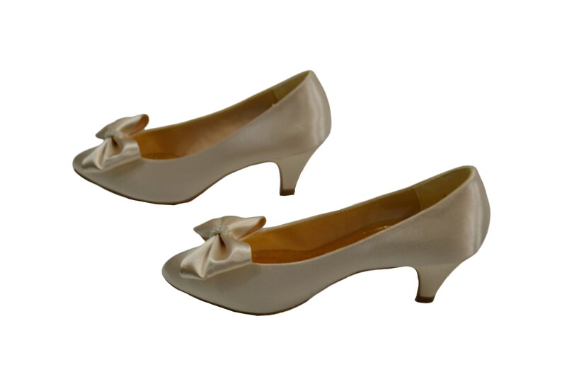 May include: A pair of ivory satin low heeled pumps with a bow detail on the toe.