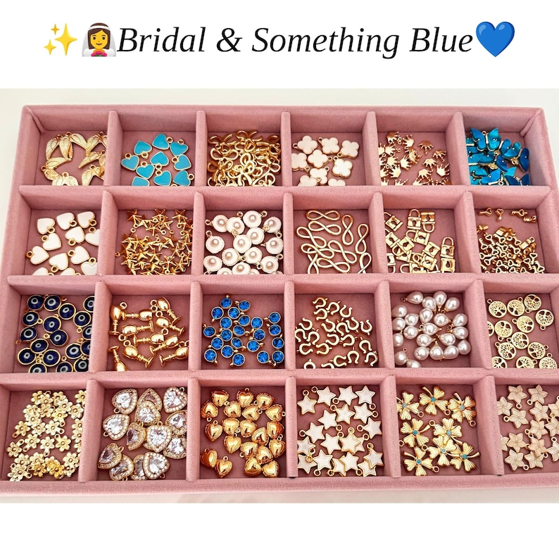 May include: A pink velvet jewelry organizer tray containing twenty-four compartments filled with various gold-tone metal charms, including blue hearts, white stars, pearls, evil eyes, and floral shapes. The text "Bridal & Something Blue" is visible.