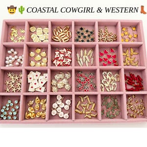 May include: A pink velvet jewelry tray with twenty compartments filled with assorted metal charms including gold cacti, cowgirl boots, seashells, stars, hearts, cherries, playing cards, and pearls. The text COASTAL COWGIRL & WESTERN is at the top.