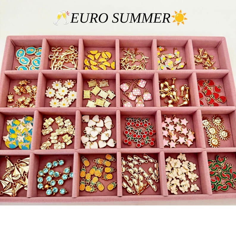 May include: A pink velvet jewelry tray with twenty-four compartments filled with assorted gold-tone metal charms. The charms feature various shapes including flowers, fruits, cameras, stars, sunglasses, and butterflies. Text reads EURO SUMMER.