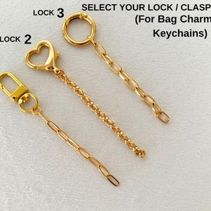 May include: Three gold-toned metal clasps with attached chains for bag charms and keychains, labeled Lock 1, Lock 2, and Lock 3. Lock 1 features a rectangular clasp, Lock 2 a heart-shaped clasp, and Lock 3 a circular ring clasp.