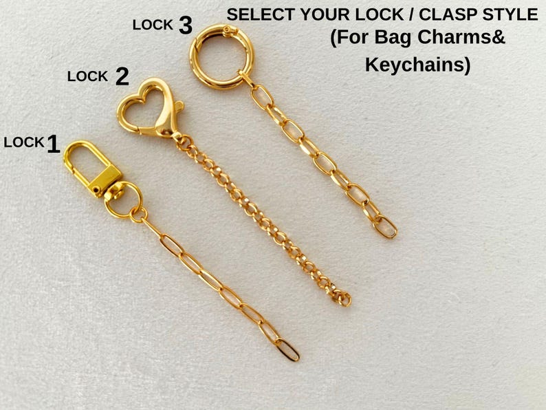 May include: Three gold-toned metal clasps with attached chains for bag charms and keychains, labeled Lock 1, Lock 2, and Lock 3. Lock 1 features a rectangular clasp, Lock 2 a heart-shaped clasp, and Lock 3 a circular ring clasp.
