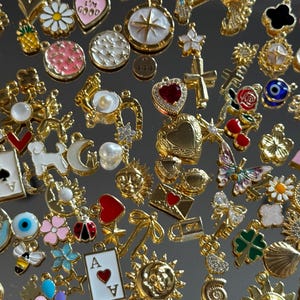May include: A collection of gold-toned charms with various designs, including hearts, flowers, playing cards, and celestial motifs. Some charms feature colorful enamel accents, such as a rainbow, blue globe, and a butterfly. The charms are arranged closely together.