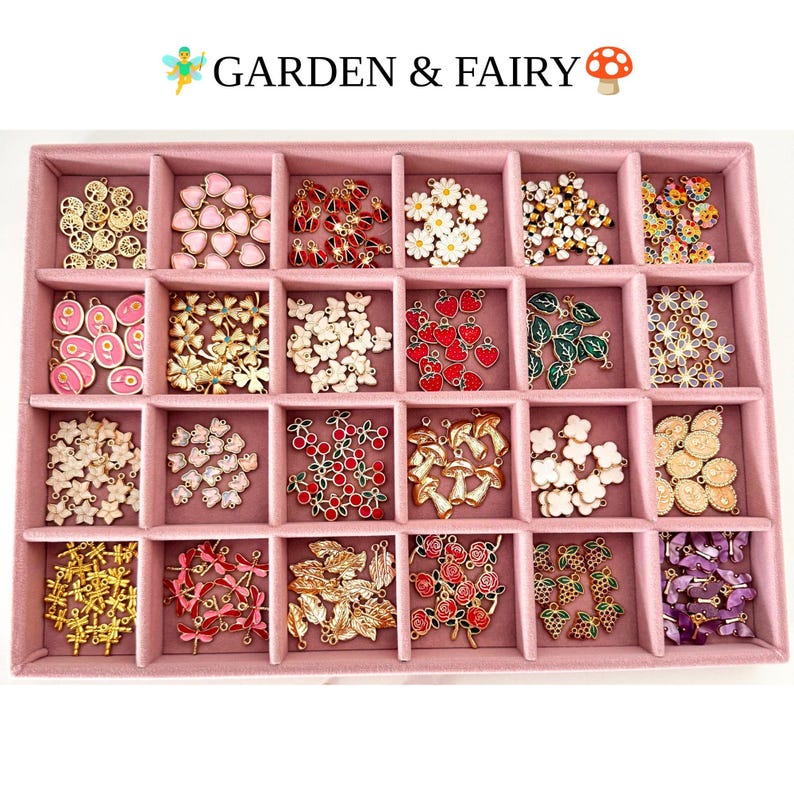May include: A pink velvet jewelry tray with twenty compartments containing various metal charms. The charms feature designs including hearts, flowers, butterflies, strawberries, mushrooms, leaves, dragonflies, and roses. Text reads GARDEN & FAIRY.