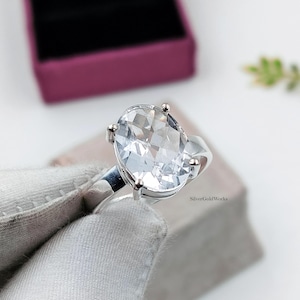 Op de afbeelding: Een zilveren ring met een grote, ovaal geslepen, heldere gefacetteerde edelsteen die door vier pootjes wordt vastgehouden. De band is van gepolijst zilver. De tekst SilverGoldWorks staat gedrukt op de zijkant van de ringzetting.