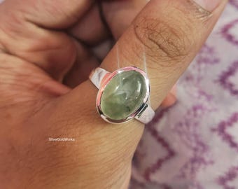 May include: A silver ring with an oval, light green gemstone. The ring has a simple band and a bezel setting. The gemstone is smooth and polished, and the ring is shown on a finger. The text "SilverGoldWorks" is visible.