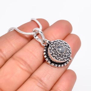 Puede incluir: Un collar con colgante redondo de plata con un diseño floral y una piedra central. El borde del colgante es de cuentas. La cadena del collar es de plata texturizada. El colgante mide aproximadamente 2,5 cm de diámetro.